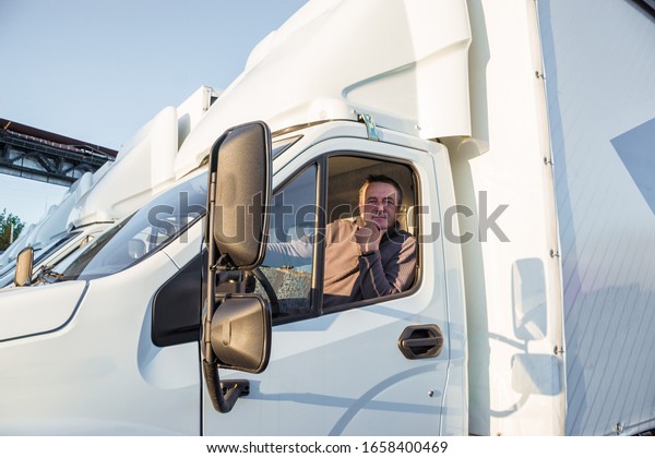 A man
driver is sitting in the cab of a modern
truck.