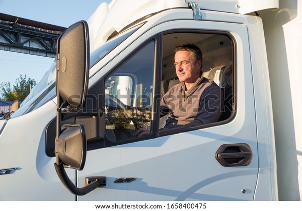 A man\
driver is sitting in the cab of a modern\
truck.