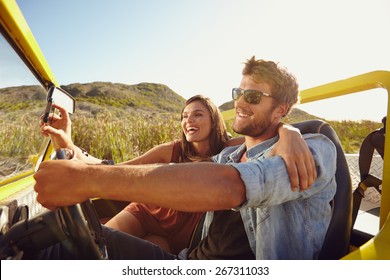 Man driving beach buggy with woman taking selfie on her smart phone. Couple having fun on road trip on a summer day. - Powered by Shutterstock