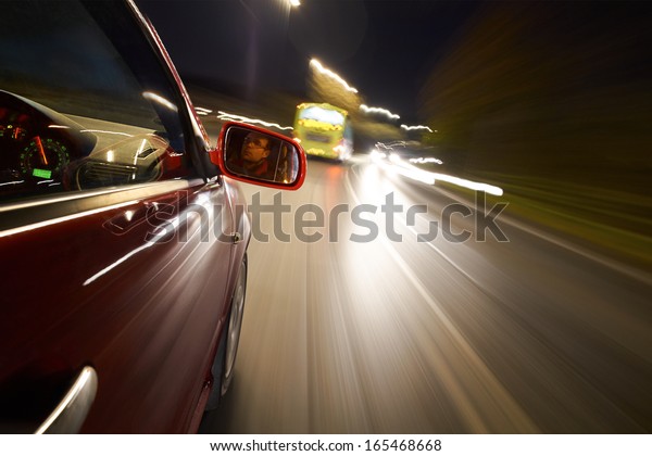 A man driving a\
car behind a bus at night.