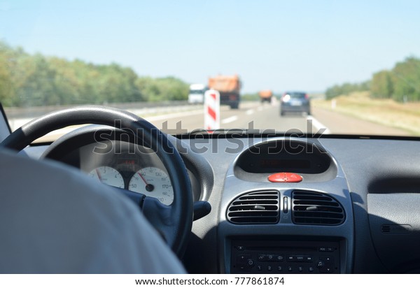 Man\
driving a car with a dirty front glass after a long drive on a\
highway and a red truck blurred in front of\
him