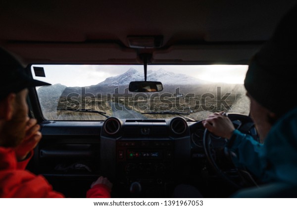 Man driving a car with a friend in the\
Highlands, Scotland