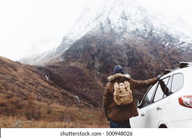 Man driving car on to the mountains. Traveler with backpack. Hiking in cold weather.