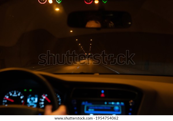 Man driving a car on a tunnel. Driver POV\
personal perspective and the front driving car in traffic jam\
exiting the tunnel.Dark highway tunnel and congested traffic.\
Driving focused and\
concentrated.