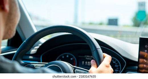 A Man Driving A Car On A Warm Sunny Day With Two Hands On The Steering Wheel.