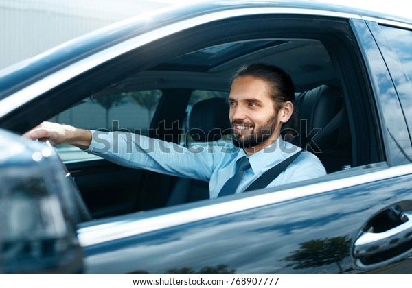 Man Driving Car. Portrait Of Smiling Male\
Driving Car. Successful Young Business Man Going To Work In\
Comfortable Auto. High\
Resolution.