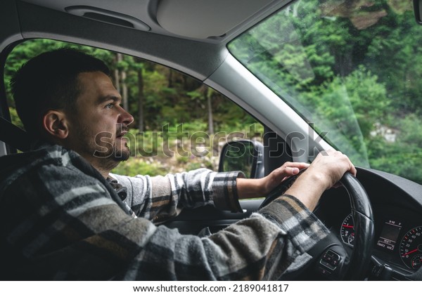A man driving a car rides in a\
mountainous forest area, a view from inside the\
car.