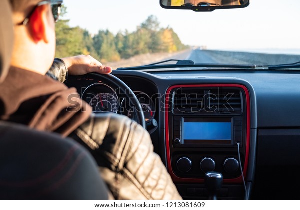 Man driving a\
car in rural area, backseat view. Male driver in modern vehicle on\
the road on a sunny\
afternoon
