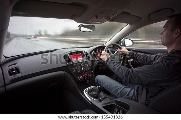 A\
man driving a car at speed in wet weather\
conditions.