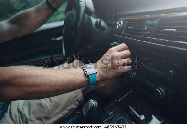 Man driving a car and tuning radio, smart watch on\
the hand