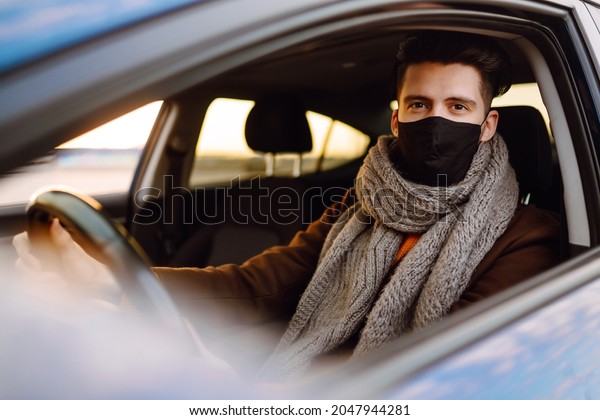 Man driving a car wearing on a medical mask\
during an epidemic, a driver in a mask, protection from the virus.\
Transport isolation.\
Covid-2019.