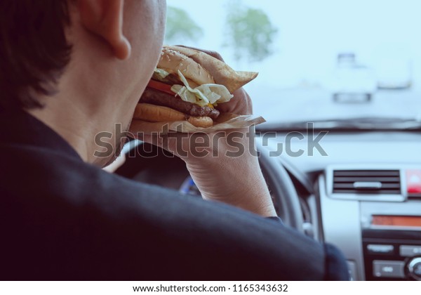 Man driving car while\
eating hamburger
