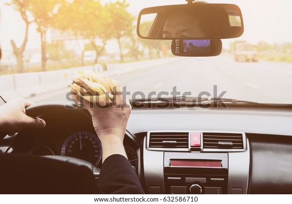 Man driving car while\
eating hamburger