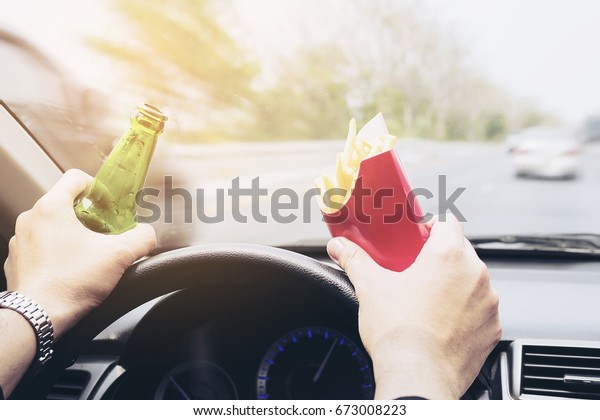 Man\
driving car while eating French fries and\
beer