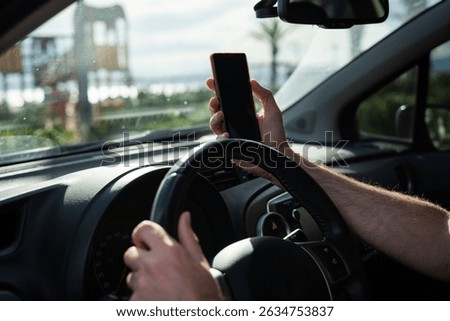 Man driving a car while using a smartphone, representing the danger of distracted driving and lack of attention on the road.