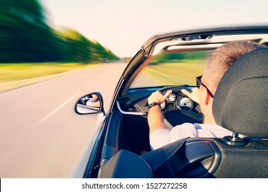 Man Driving A Convertible Car On Country Road. View From The Inside Behind The Driver. Man Is Driving At High Speed On The Highway. Dangerous Fast Driving. Motion Blur Effect