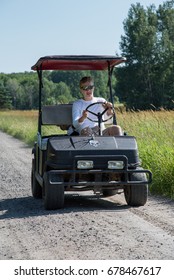 Man Driving A Custom Golf Cart Down A Gravel Road, Canada. 