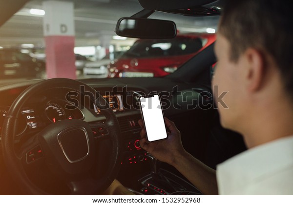 Man driving holding smartphone in car. Blank\
screen of smartphone on\
parking