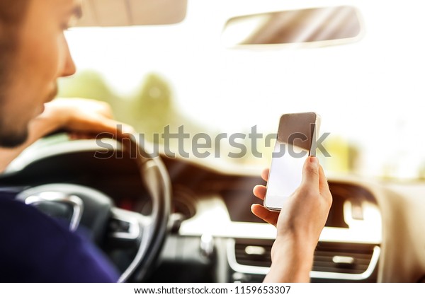 Man driving\
luxury car and looking at mobile or cell phone.  Vehicle expesive\
dashboard in background\
blured.
