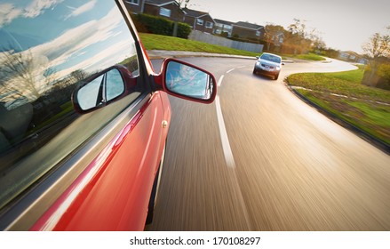 A Man Driving A Red Car Towards A Bend In The Road.