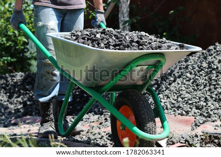 Man driving a wheelbarrow with crushed stones, as part of a building project