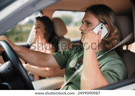 Man driving while using smartphone with a woman passenger in a relaxed interior