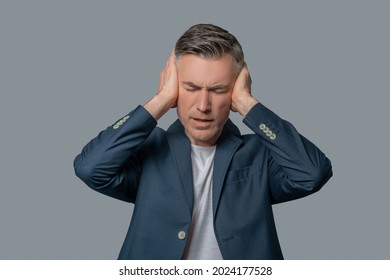 Man with drooping eyelids covering ears with hands - Shutterstock ID 2024177528