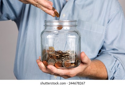 Man Drops Money Into A Glass Jar For A Savings Account.