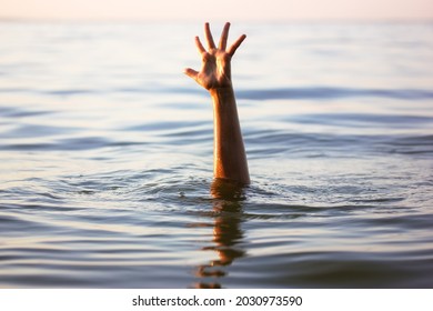 A man is drowning in water. A hand peeks out from under a water. A drowning person needs help, rescue. A risk, danger for living in the sea, river, ocean, pond. Death, SOS concept. Drowning victim