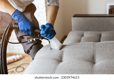 Man dry cleaner's employee hand in protective rubber glove cleaning sofa with professionally extraction method. Early spring regular cleanup. Commercial cleaning company concept. Closeup