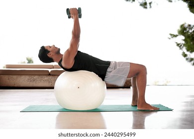 Man, dumbbell and exercise ball on yoga mat or flexibility training for healthy mobility, fitness or weightlifting. Male person, equipment and workout strength for sport challenge, gym or balance - Powered by Shutterstock