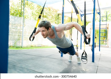 Man During Workout With Suspension Straps On The Street. Trx