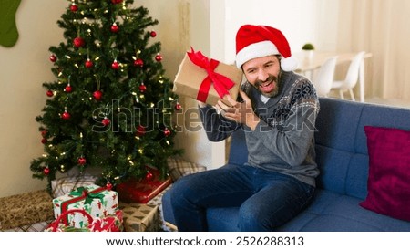 Man eagerly shaking a christmas present and guessing its contents while seated on a festive sofa in a beautifully decorated living room