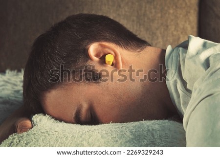 Man with earplugs lying in bed. Daytime sleep. rest, Siesta. Yellow ear plugs in the ears of a young boy sleeping in the afternoon on the couch when prevent sleep.