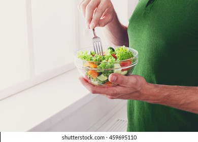 Man Eat Healthy Lunch In Modern Interior. Unrecognizable Profile Male Torso In Green T-shirt, Hand With Fork, Near Window With Vegetable Salad In Bowl, Diet Food Concept. High Key Image