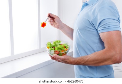 Man Eat Healthy Lunch In Modern Interior. Unrecognizable Profile Male Torso In Blue T-shirt, Hand With Fork, Near Window With Vegetable Salad In Bowl, Diet Food Concept. High Key Image