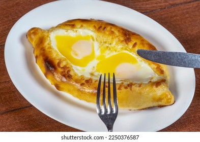 Man eating adjar Khachapuri. Georgian national pie khachapuri with egg and cheese in the white plate  on wooden background. - Shutterstock ID 2250376587