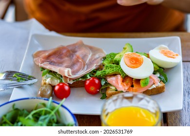 Man Eating Breakfast Toast With Egg.Toast For Breakfast.Breakfast In The Hotel.Home Cooked Healthy Food.Toast With Avocado, Arugula And Ham.Avocado Toast.Lunch At Work.Breakfast Outside.Orange Juice