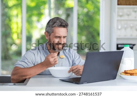 Man eating breakfast while managing online work. Morning home office. Man eat morning breakfast in kitchen. Man having milk coffee. Freelancer eating and working at home
