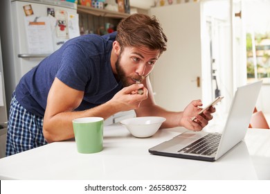 Man Eating Breakfast Whilst Using Mobile Phone And Laptop - Powered by Shutterstock