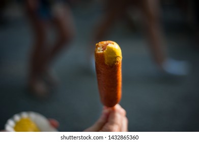 Man Eating Corn Dog With Mustard In Theme Park