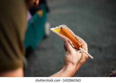 Man Eating Corn Dog With Mustard In Theme Park