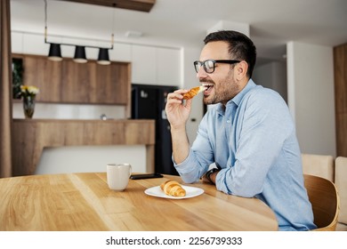 A man eating croissant for breakfast at home. - Powered by Shutterstock