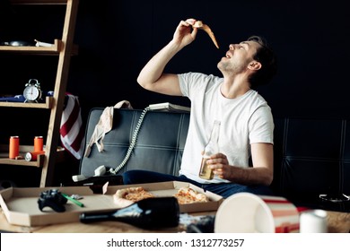Man Eating Delicious Pizza While Holding Bottle In Messy Living Room