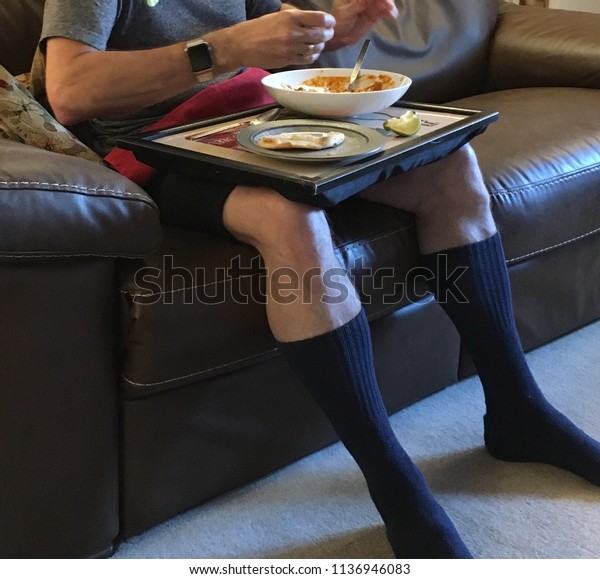 Man eating dinner on a tray whilst\
watching TV symbolising the growing trend to eat dinner in front of\
the TV instead of around a table with the\
family