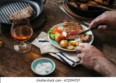 Man is eating dinner at a wooden table. Grilled steak with potatoes and salad
