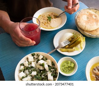 Man Eating Fresh Warm Hummus With Pita Bread, Pickles, Feta Cheese Salad With Organic Herbs And Drinking Fresh Squeezed Fruit Juice. Healthy Eating Middle Eastern Cuisine Background.  Foodie Travel.