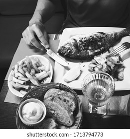 Man Eating Grilled Fish In Traditional Seaside Restaurant In Normandy, France. Top View Food Background. Healthy Diet, Eat Local, Zero Km Food, Foodie Concepts. Black White Historic Photo.