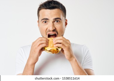 Man eating a hamburger on an isolated background and a white T-shirt cropped view