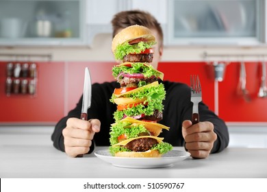 Man Eating Huge Burger At Table